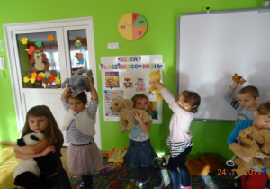 Dzieci tańczą po kole z misiami w górze.